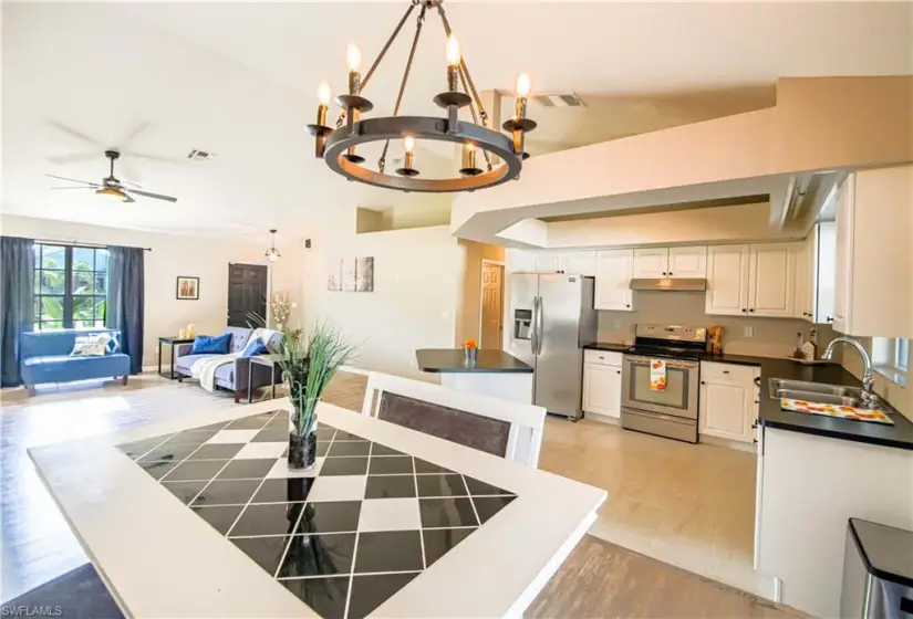 Kitchen with light wood-type flooring, ceiling fan with notable chandelier, range with electric cooktop, stainless steel refrigerator with ice dispenser, and sink